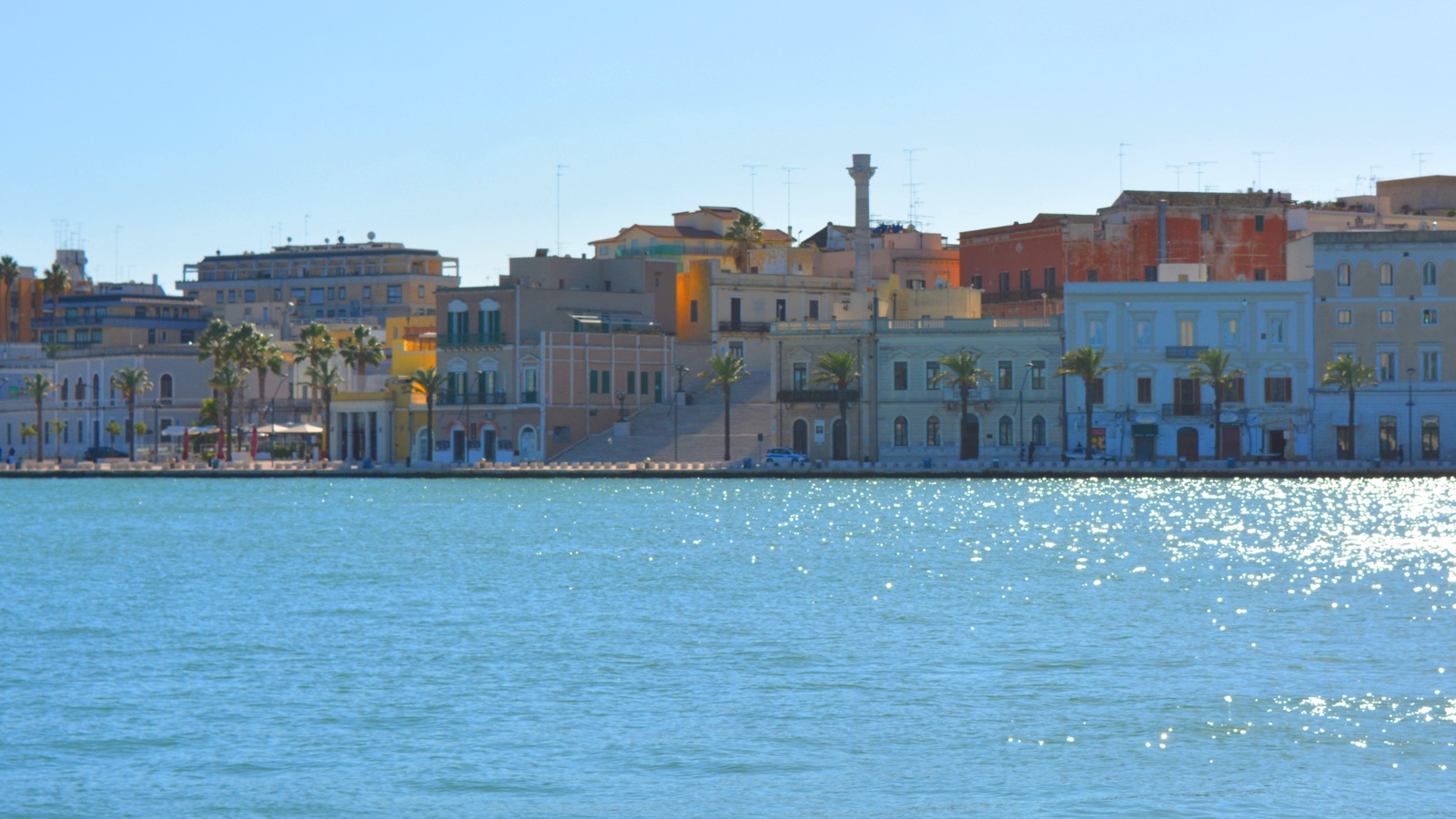 Il lungomare di Brindisi visto dal porto interno: facciate colorate, palme e la colonna romana.