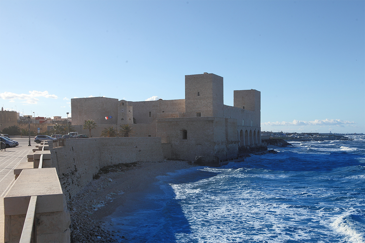 Il Castello svevo di Trani a filo d’acqua, con le torri quadrate e il mare mosso in primo piano.